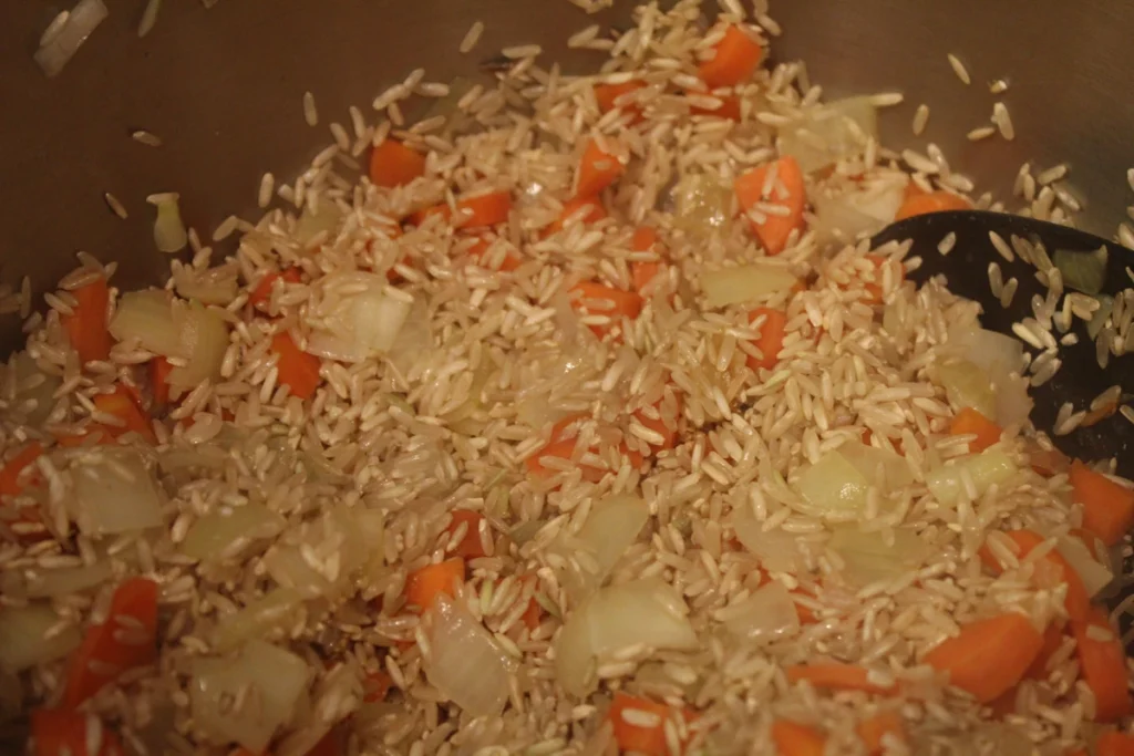 toasting rice in a pot with diced onion and carrot.