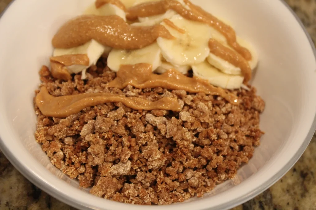 Bowl of sourdough grape-nuts topped with bananas and peanut butter.