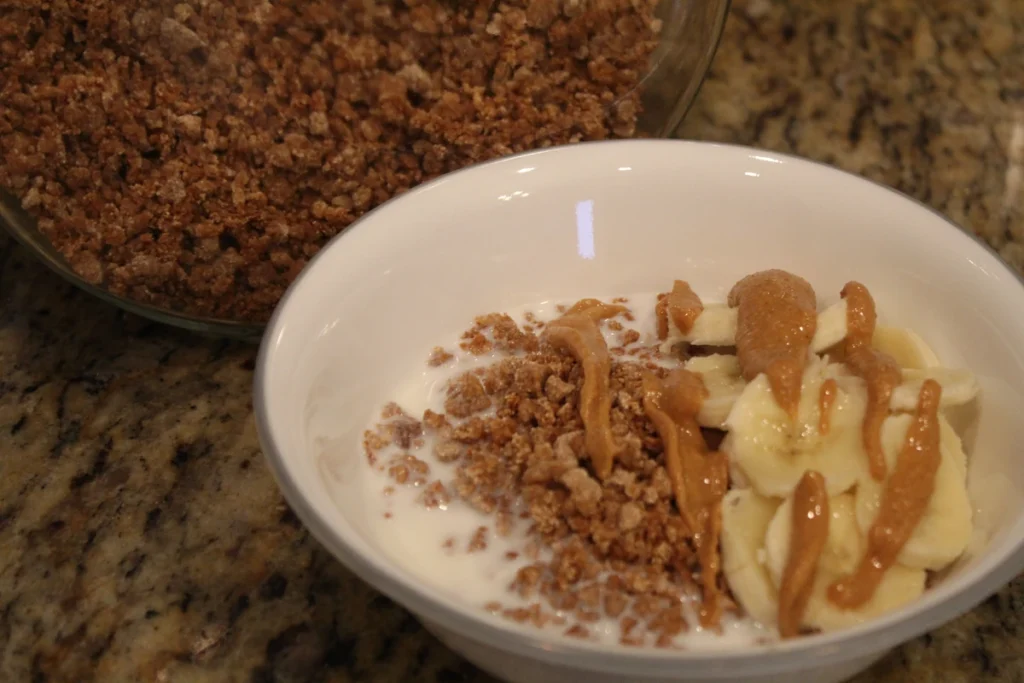 Bowl of sourdough Grape-nuts topped with milk bananas and peanut butter in front of a jar of grape nuts.