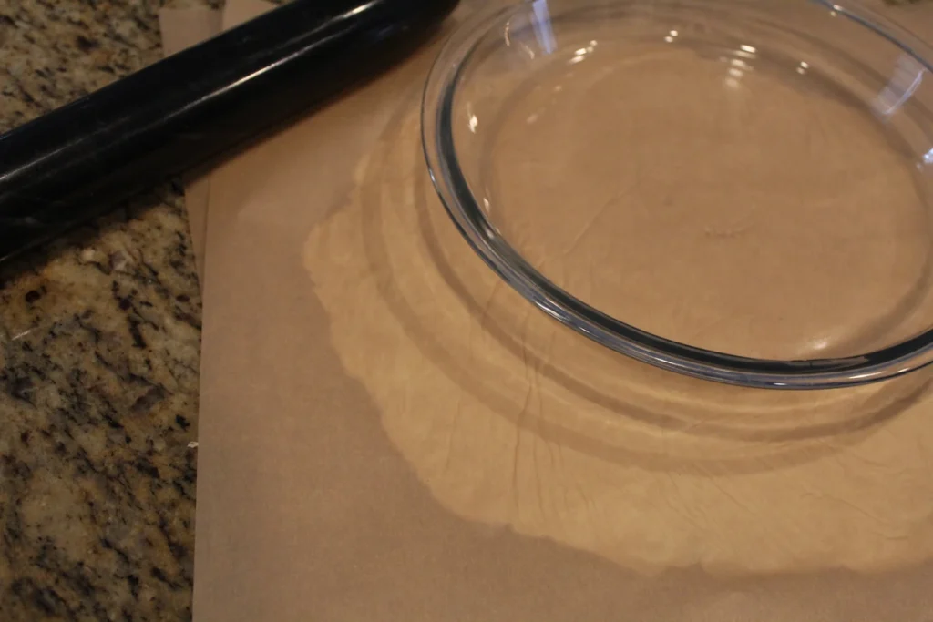 Rolling out pie crust, between pieces of parchment paper, to the size of a pie plate.