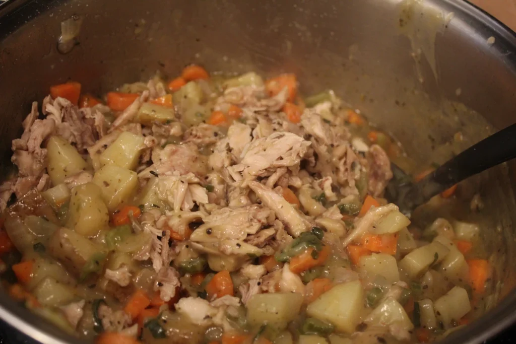 Adding chicken to thickened pot pie filling.