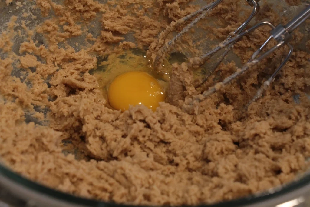 Adding an egg to beaten butter and sugars.