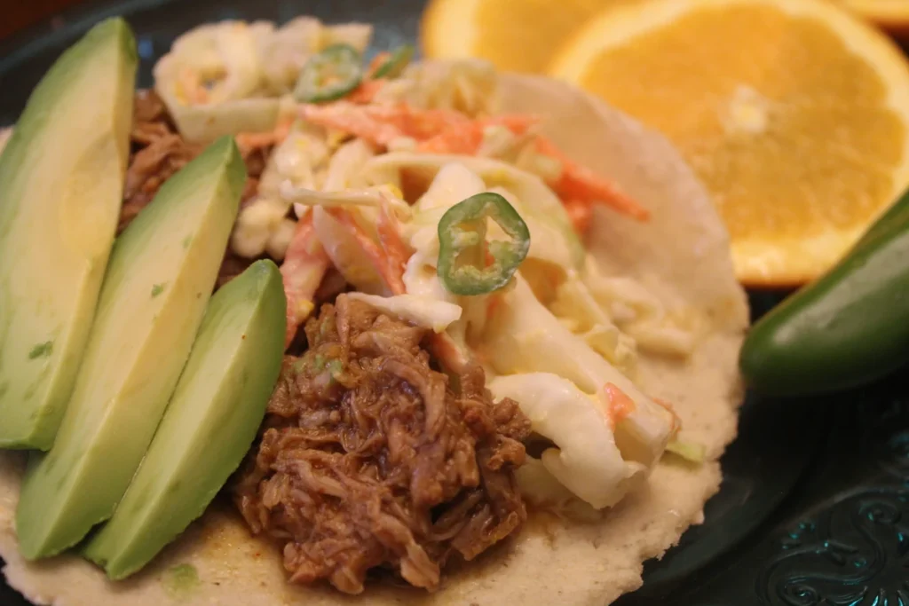 Citrus pork taco topped with avocado, and slaw, with orange slices and jalapeno.