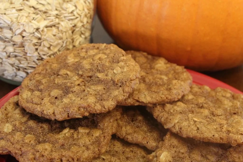 plate of pumpkin spice oat cookies with pumpkin and oats in the background.