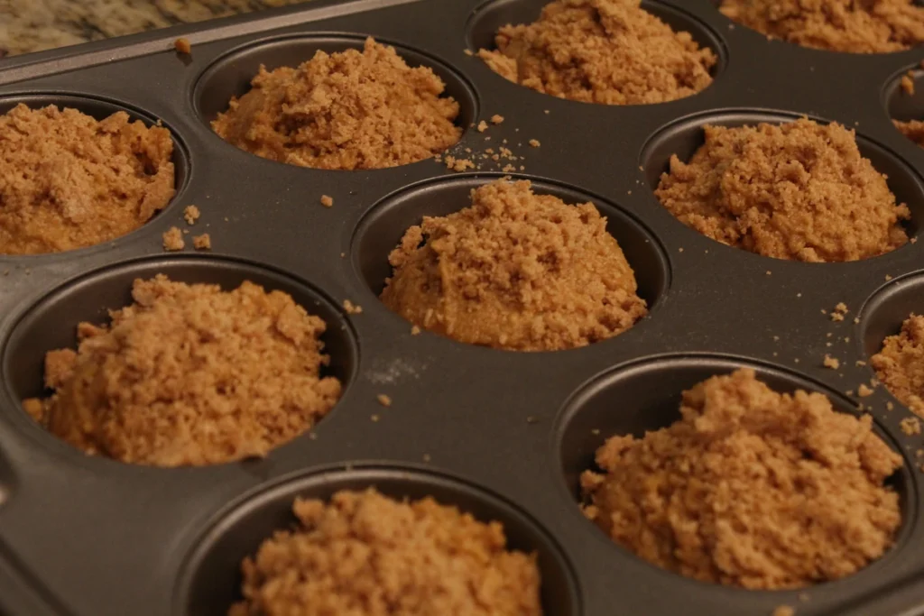Muffin batter in a muffin tin topped with struesel.