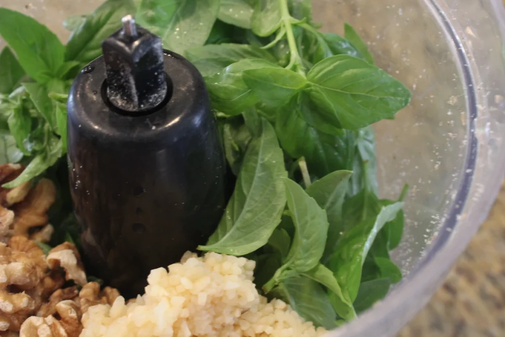 Close up of fresh basil, minced garlic and walnuts in a food processor