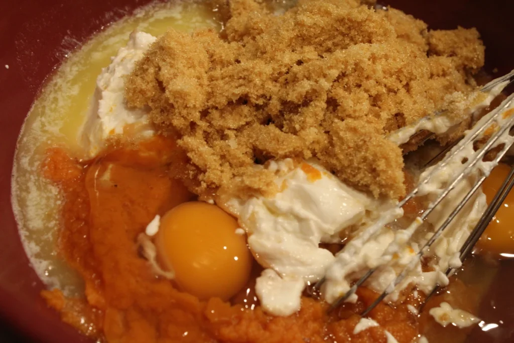 Melted butter yogurt brown sugar and eggs in a mixing bowl with a whisk.