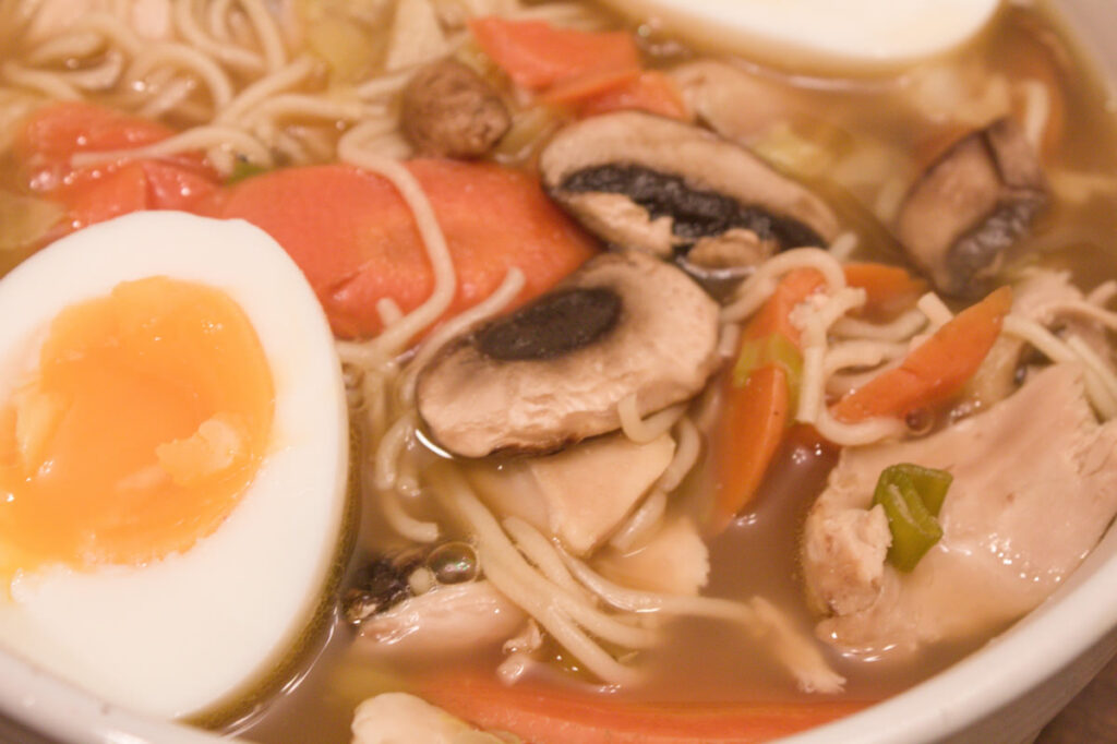 close up of a bowl of ramen with chicken, mushrooms carrots and a soft boiled egg.