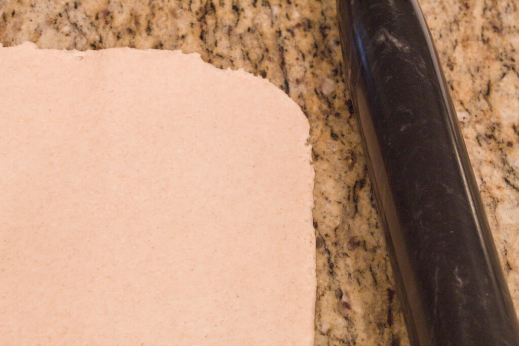 Dough rolled out into a rectangle next to a black marble rolling pin.