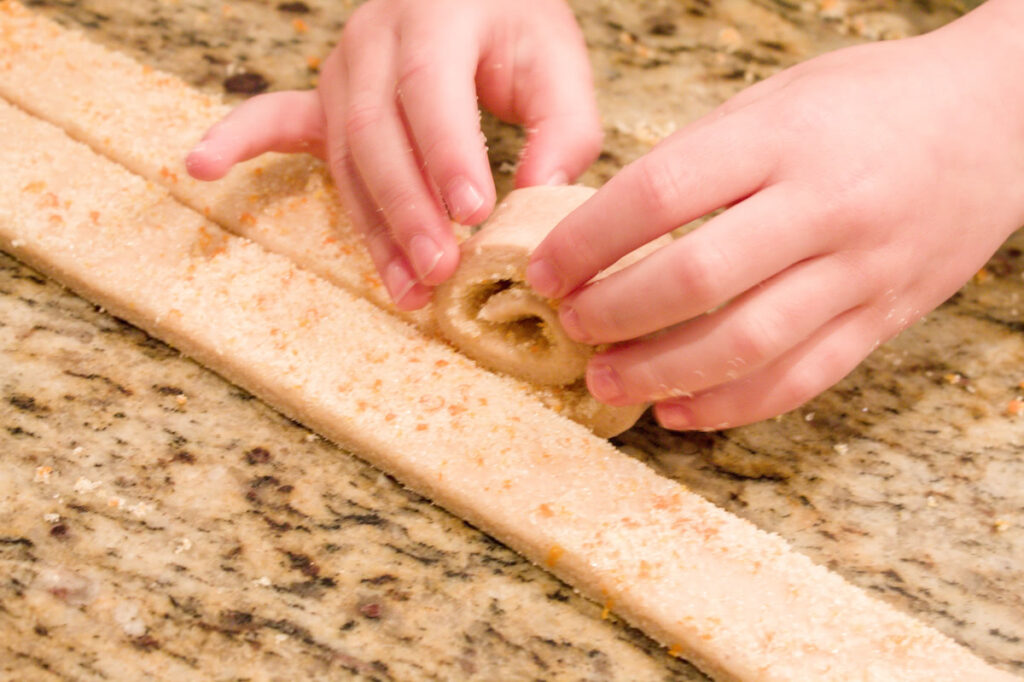 A child's fingers rolling dough into an orange roll.