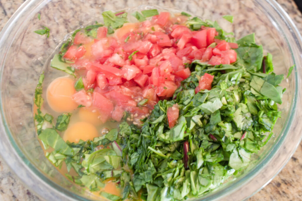 finely chopped tomatoes and greens on top of eggs in a bowl.