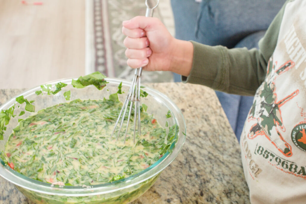 Child's arm whisking together quiche filling.